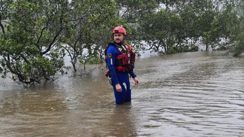 An emergency responder knee deep in floodwater in Urunga, New South Wales