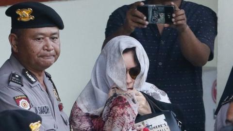 Schapelle Corby in sunglasses with a scarf over her head and part of her face, surrounded by police