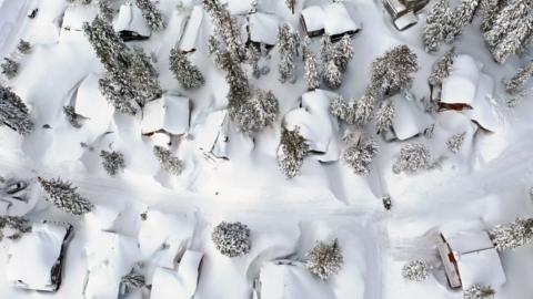 In an aerial view, snow covers roofs next to snowbanks piled up from new and past storms in the Sierra Nevada mountains, in the wake of an atmospheric river event, on March 12, 2023 in Mammoth Lakes, California