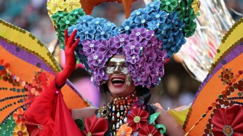 A participant is seen in a huge elaborate rainbow-themed butterfly costume