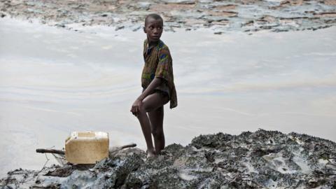 A boy with a fishnet standing on the oil stained bank of a creek near Goi, Ogoniland, Nigeria