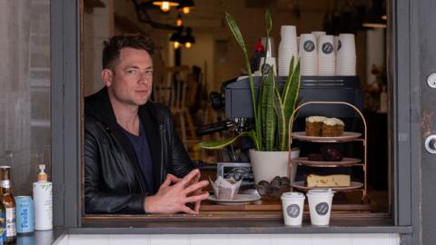 Matt Lanigan sits in his takeaway shop window next to a coffee machine