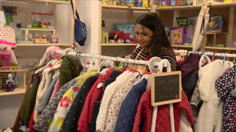 A woman arranges colourful children's coats on a rail