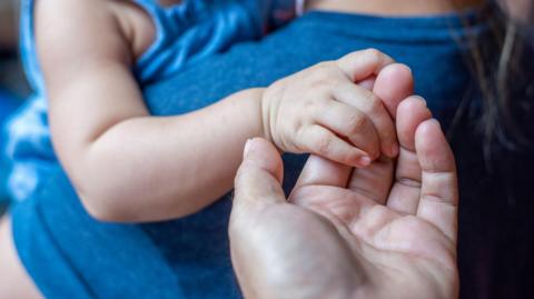 A toddler in an electric blue dress holds an adult's hand.