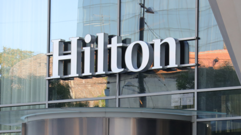 A glass-fronted building with a large white sign which reads Hilton