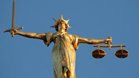 A statue, depicting someone holding a sword in their right hand, in front of a blue-sky background.
