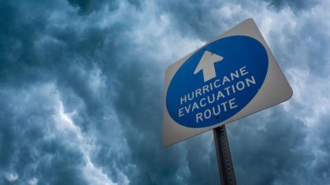 Blue and white hurricane evacuation sign against a stormy sky