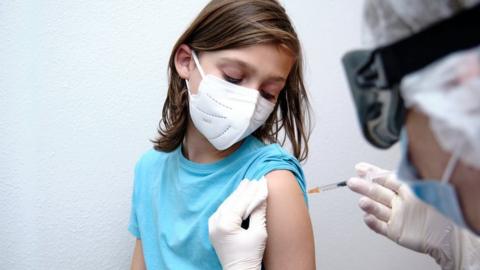 child in blue t-shirt and mask gets vaccine