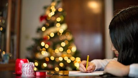 Child writing in front of Christmas tree