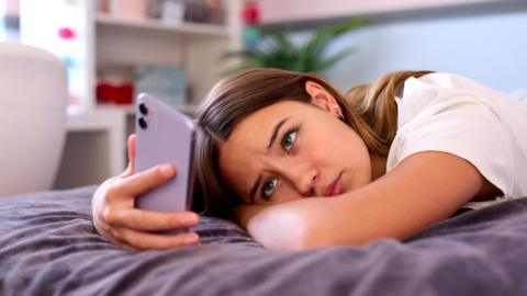 Teenage Girl Lying On Bed At Home Looking At Mobile Phone