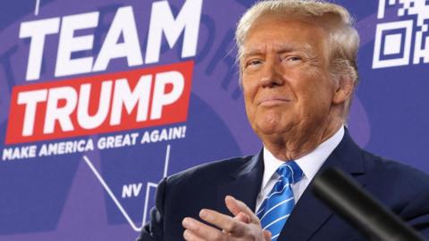 Donald Trump in front of a sign that reads "Team Trump"