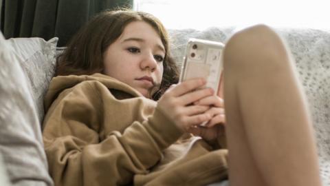 Stock image of a teenager sat on a sofa looking at their phone