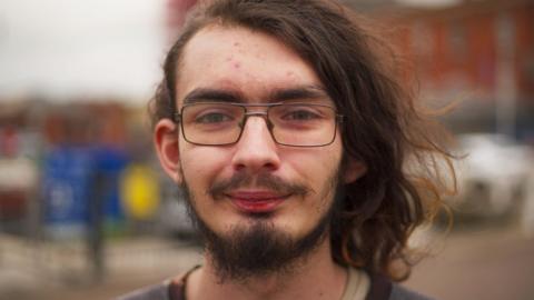 Kye Bourne, a young man with long hair, glasses and a beard outside Gloucester docks