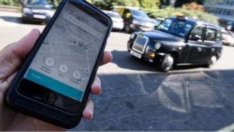 An Uber app is help in front of a black cab taxi