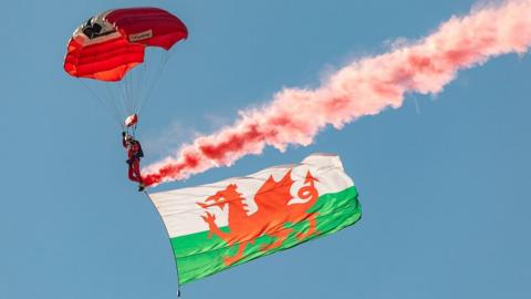 A red devil parachuting with a Welsh flag