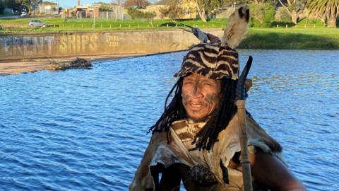 Man in traditional dress standing in front of some water