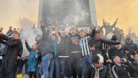 A large group of Newcastle fans dance and sing around the base of Nelson's Column