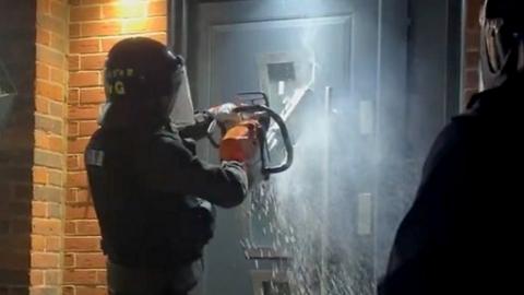 Essex Police use a chainsaw to cut through a door during a raid