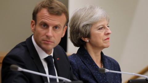Emmanuel Macron, facing the camera, beside Theresa May, who is facing away