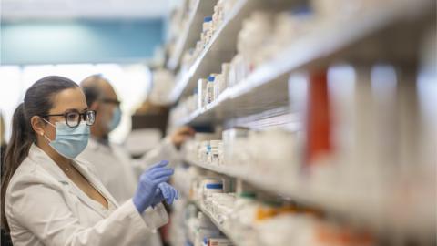 Pharmacist working at a pharmacy organizing products while wearing a protective face mask during the coronavirus outbreak.