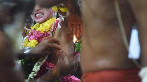 A boy cringes as his skin is pierced with a hook.