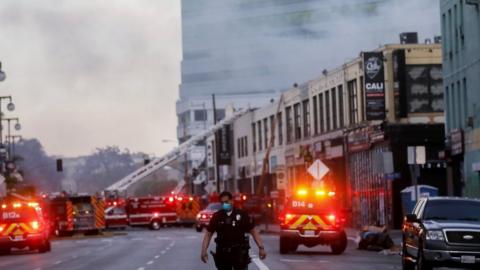 An LAPD officer keeps watch on a multiple structure fire as LAFD firefighters work following an explosion on May 16, 2020 in Los Angeles, California