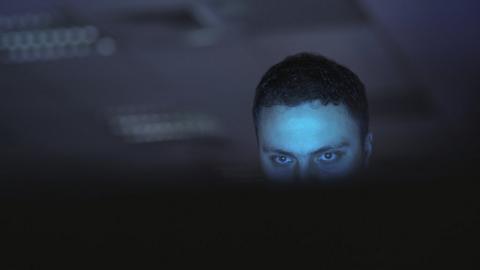 A shadowy figure using a computer - stock image