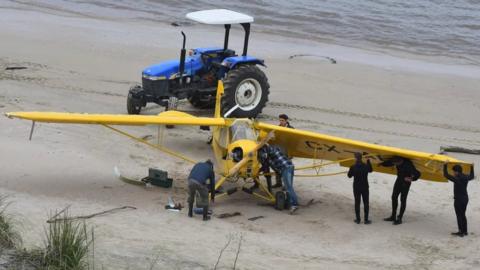 People inspect the yellow plane on the beach