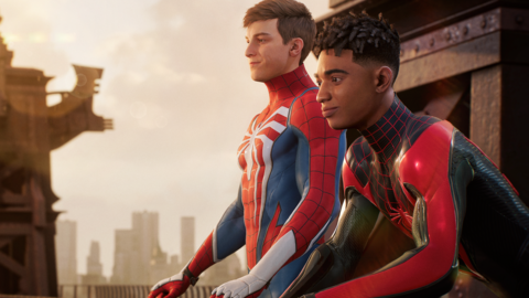A screenshot from Spider-Man 2 showing protagonists Peter Parker and Miles Morales sitting on a balcony. They're both wearing their figure-hugging Spidey Suit costumes, but neither is wearing a mask. Peter's suit is mostly red, with thin black lines suggesting a spider's web. It also has blue panels on the biceps, triceps and flanks of his torso. A large, white, spider decal is printed on his chest, its legs extending to the edges of the suit. Peter is white, with fairly short, neatly cropped hair. Mile's suit has a similar design but is mainly black, with red panelling, web lines and spider decal. He's a young black man with short, afro-style hair style in locs. Both look out over New York contemplatively.