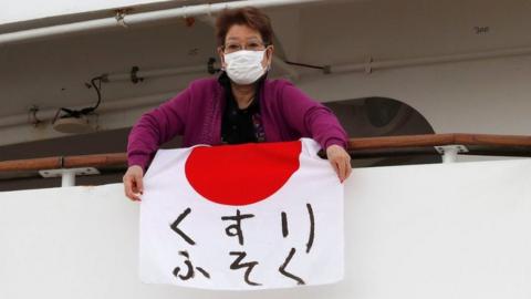 Woman waving a flag reading "shortage of medicine" from the ship