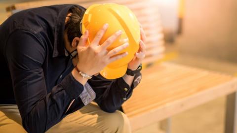 Man in yellow hard hat with his head in his hands