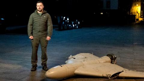 President Volodymyr Zelensky stands beside a downed drone