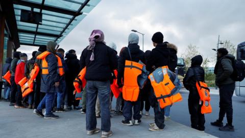 Migrants waiting for a bus to return from beach to their camp in Calais after people died in an attempt to cross the English Channel on Tuesday