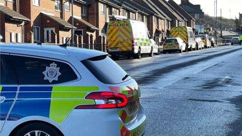 Police car in foreground with further emergency vehicles in the background, at the scene of a fatal crash