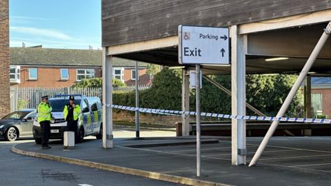 A police cordon and police van next to the car park