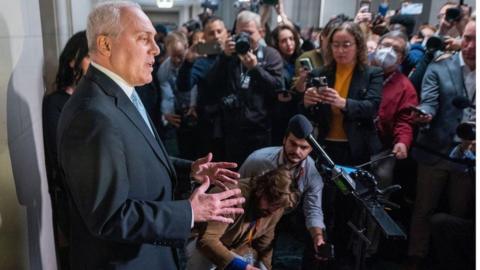 Steve Scalise in dark suit, hands raised, before reporters holding up phones and microphones.