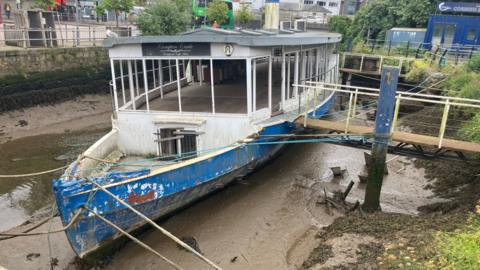 A derelict boat sits on the silt in. riverbed.
