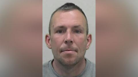 Mugshot of Batey. He has faint stubble and short dark hair.