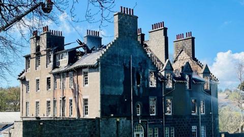 Firefighters in a height vehicle using water to dampen down the shell of a building hit by fire.