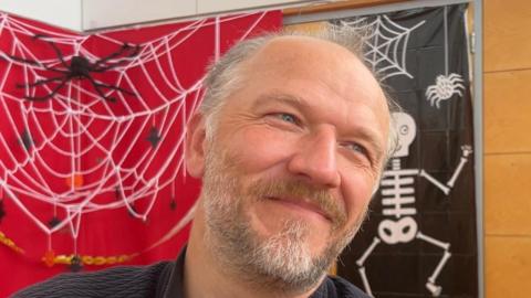 Man smiling in front of image of skeleton and web.