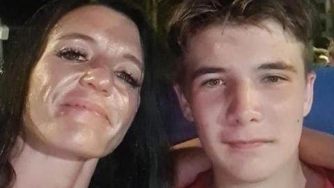 A close-up of Kirsten Coutts with her arm around her son, Sam. She has long black hair and he has short brown hair, both have the same coloured hazel eyes. They are smiling at the camera.