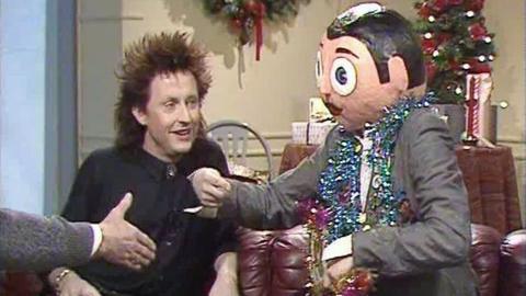 Frank Sidebottom sits beside a man on a sofa