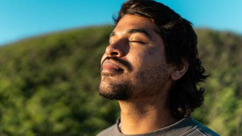 A man with his eyes closed against a green and blue background