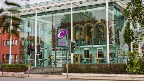 An external view of the Capitol Theatre in Horsham. There is a road in front of the theatre and steps leading to a large glass building. 