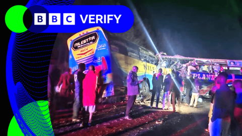 People standing in front of two buses which have crashed. Both vehicles have sustained heavy damage