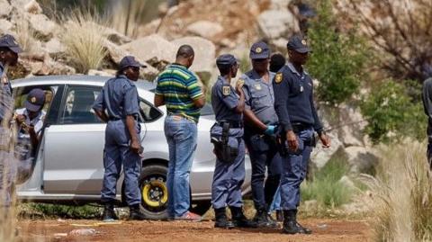 Police officers wearing blue uniform stand around at the entrance of a mine shaft where 4,500 illegal miners are trapped underground - 13 November 2024