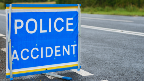 A blue and white sign reading Police Accident is erected at the side of a main road