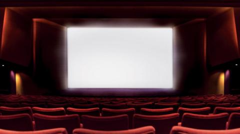 A blank cinema screen with rows of red chairs in the foreground