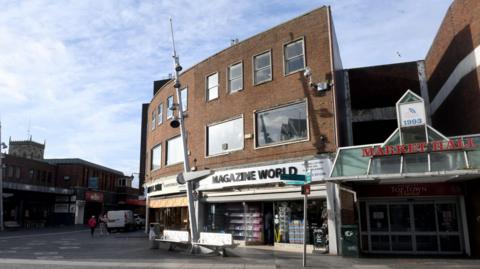 A building can be seen on the right with the red wording of "Market Hall" at the top. Below it says "Top Town Market". It is next to a shop called Magazine World, and a Wilko is across the street