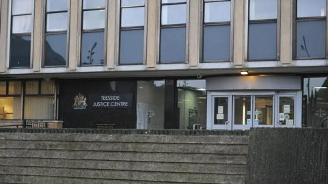 Exterior of the grey-concrete court building. A sign next to the glass doors reads: "Teesside Justice Centre".